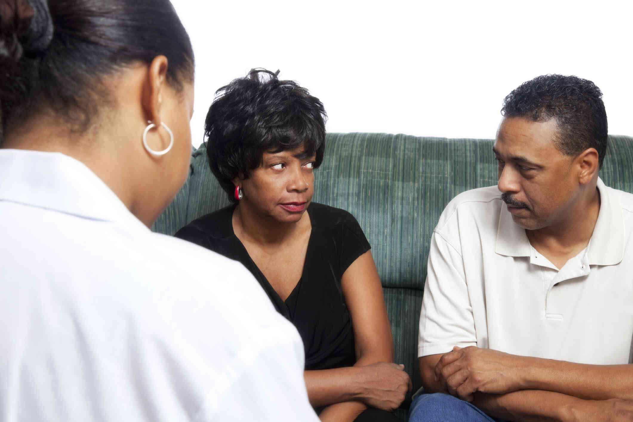 A woman and her male partner look at each other while sitting on a couch across from their female therapist during a therapy session.